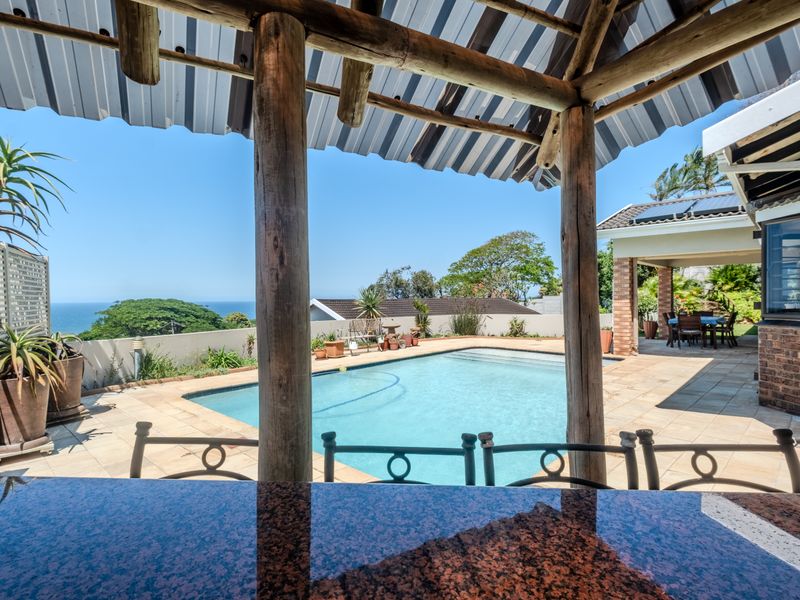 Outdoor entertainment area featuring a swimming pool, paved patio, and a covered bar area with granite countertop and scenic coastal views.