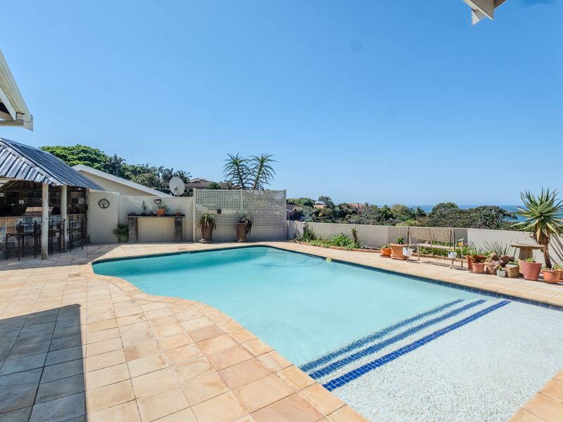 Outdoor pool area featuring a tiled surround, covered patio with a built-in bar, and scenic coastal views.
