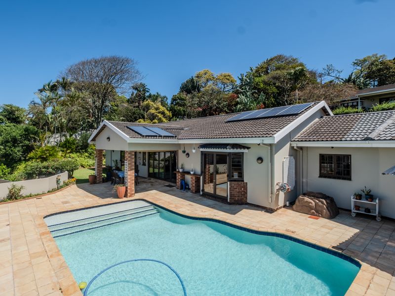 Rear exterior view of the townhouse featuring a swimming pool, tiled patio area, and roof-mounted solar panels set against a landscaped garden.