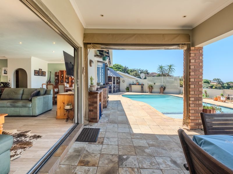 Covered patio area featuring tiled flooring and brick pillars, seamlessly connecting to the indoor living space and overlooking the private swimming pool.