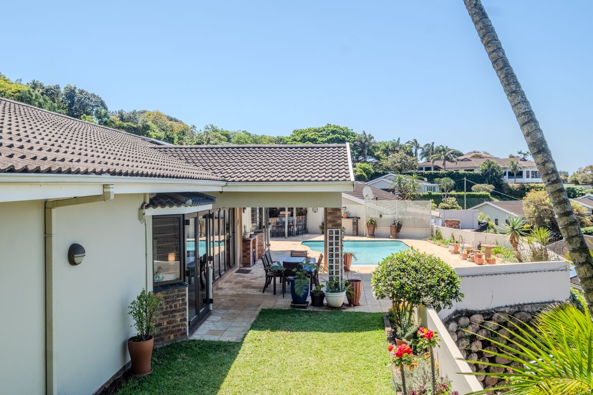 Rear view of the townhouse featuring a covered patio, paved terrace, and a swimming pool set within a landscaped garden.
