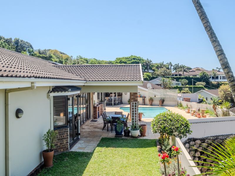 Rear view of the townhouse featuring a covered patio, paved terrace, and a swimming pool set within a landscaped garden.