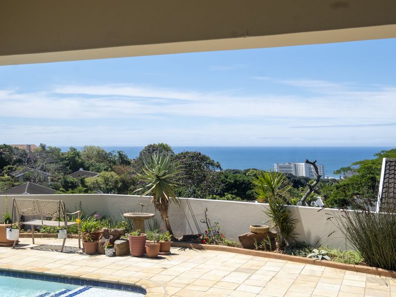 A sunny outdoor pool area featuring a tiled patio and masonry boundary wall, offering expansive coastal and ocean views.