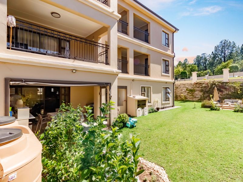 Rear view of the apartment building featuring a ground floor patio, upper-level balconies with iron railings, and a well-maintained private garden area.