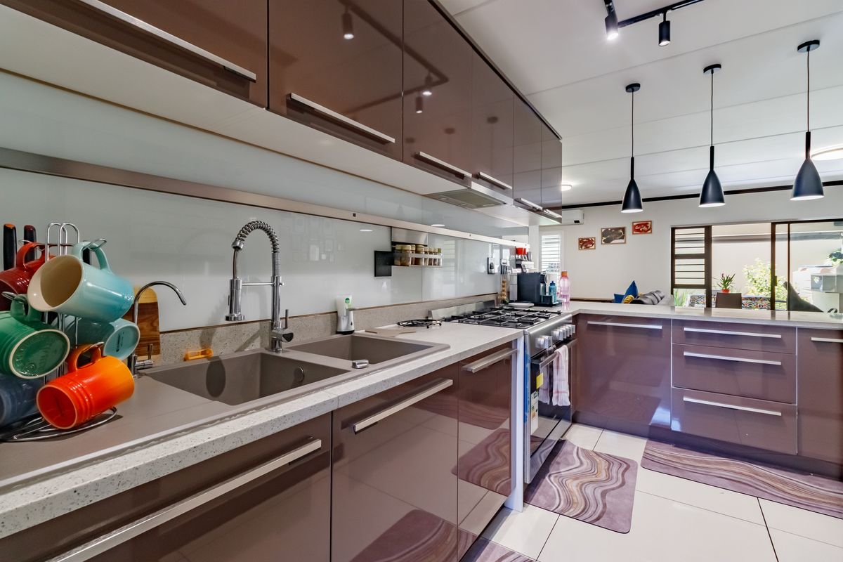 Modern kitchen featuring high-gloss cabinetry, stone countertops, a double basin sink with a gooseneck faucet, gas hob, and stylish pendant lighting.