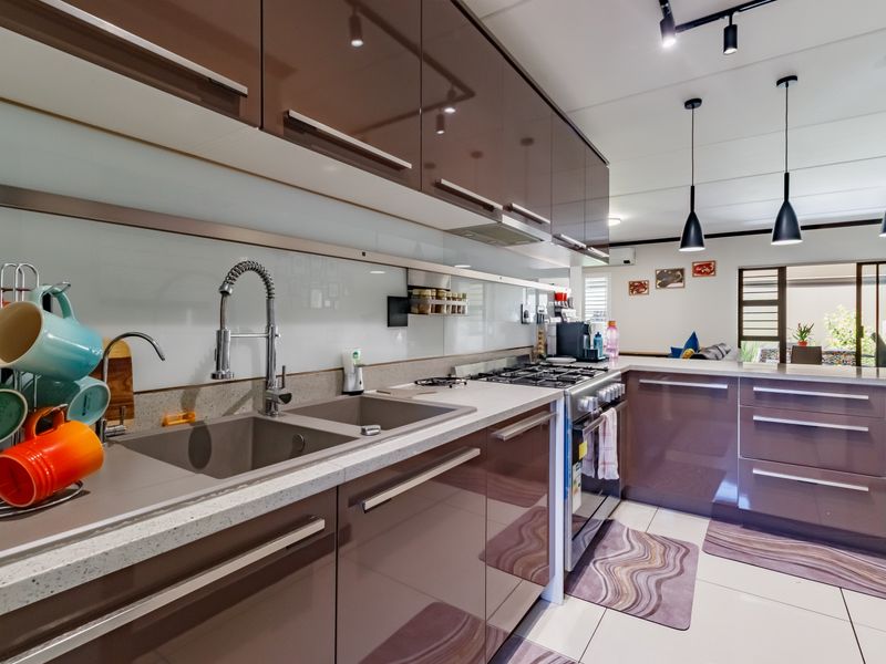 Modern kitchen featuring high-gloss cabinetry, stone countertops, a double basin sink with a gooseneck faucet, gas hob, and stylish pendant lighting.