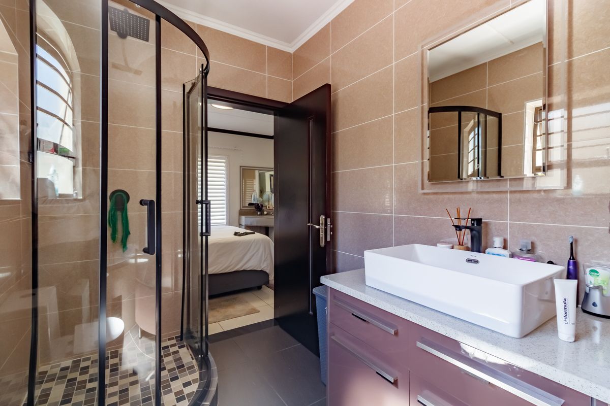Modern bathroom featuring a corner shower enclosure, vanity cabinet with a vessel sink, and neutral wall tiling.