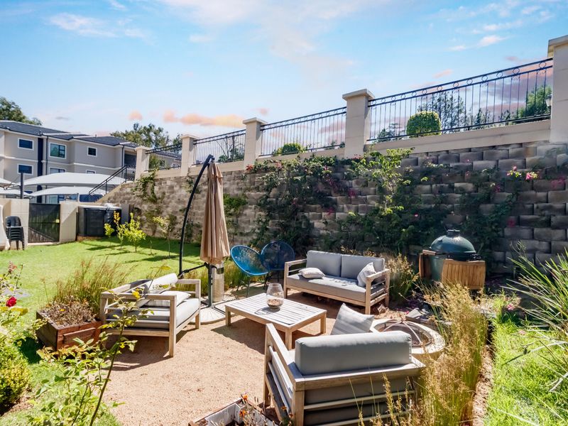 A well-maintained private garden featuring a paved patio area, lush lawn, and a decorative retaining wall with integrated wrought iron fencing.