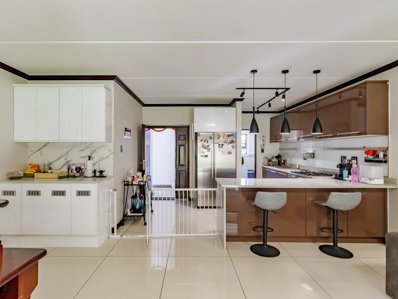 Modern kitchen featuring high-gloss cabinetry, stone countertops, a breakfast bar, and integrated appliances, complemented by stylish pendant and track lighting.