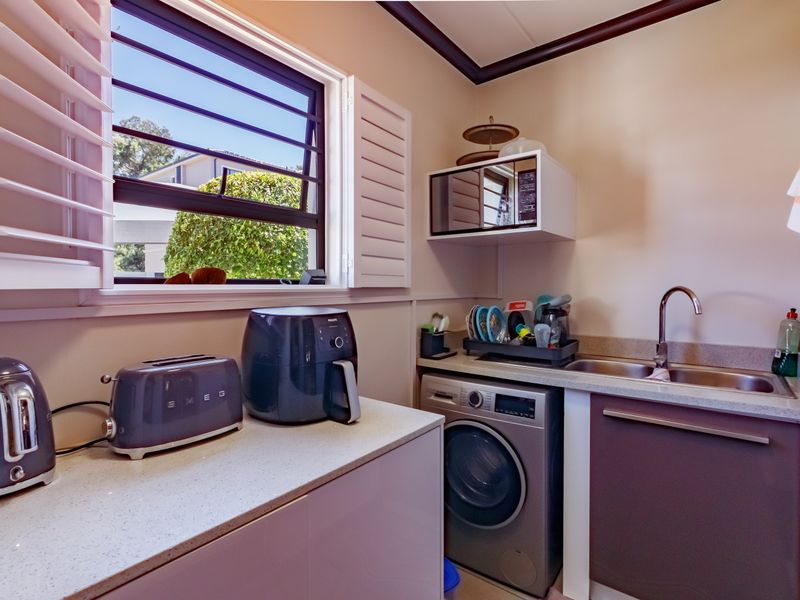 A functional scullery area featuring built-in cabinetry, stone countertops, a stainless steel sink, and integrated microwave space, providing efficient utility and prep storage.