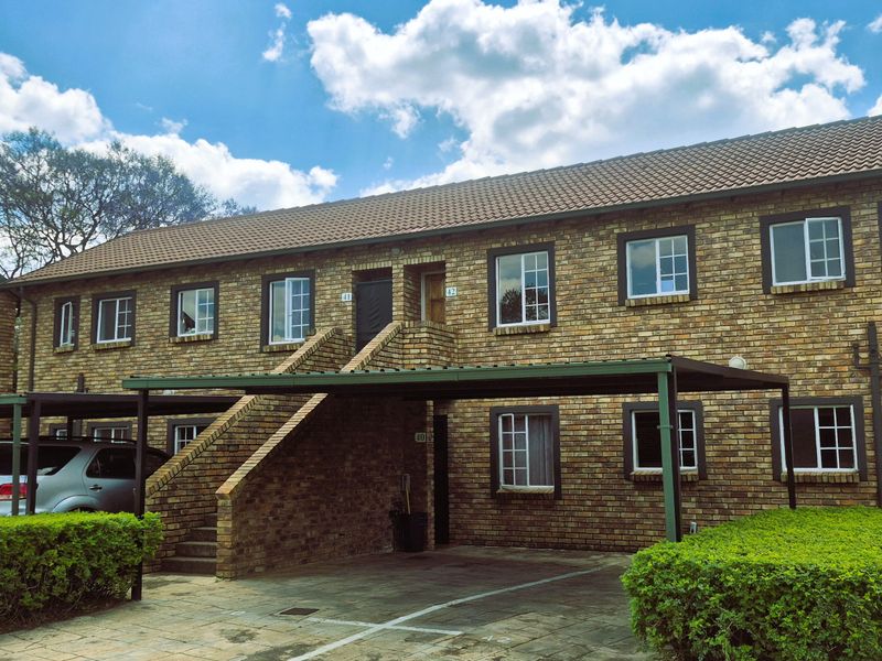 A two-story face brick apartment complex featuring a tiled roof, external staircase access, and dedicated covered carport parking spaces.