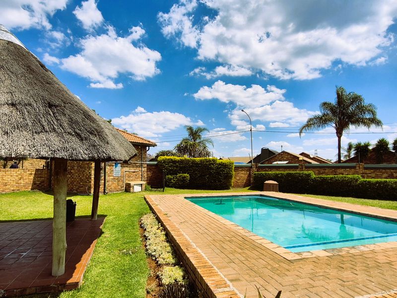 Outdoor pool area featuring a swimming pool, brick paving, and a traditional thatched lapa set within a well-maintained garden and perimeter wall.