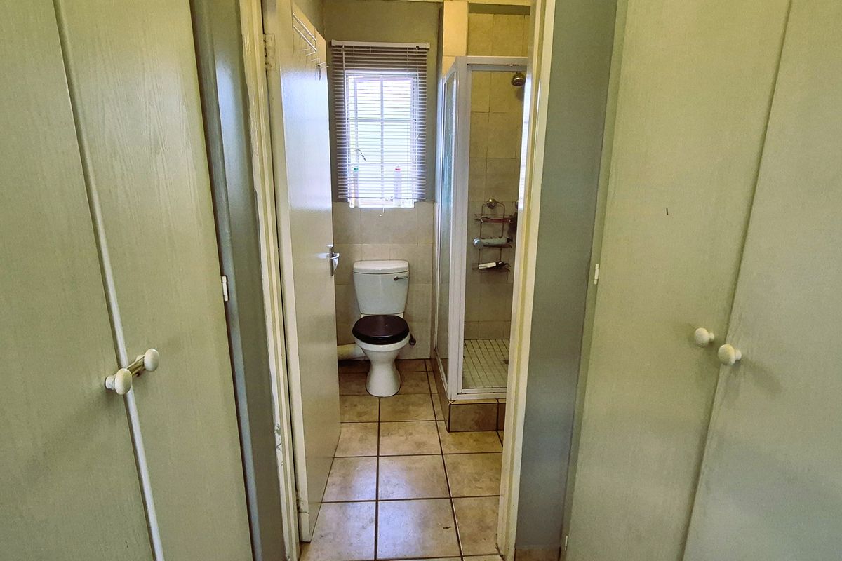 A functional bathroom featuring built-in storage cupboards, a separate shower enclosure, and a toilet, with neutral tiled flooring throughout.