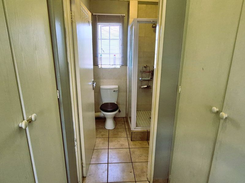 A functional bathroom featuring built-in storage cupboards, a separate shower enclosure, and a toilet, with neutral tiled flooring throughout.