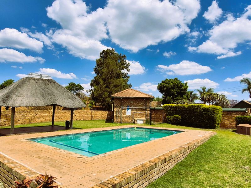 Communal pool area featuring a swimming pool, brick paving, and a traditional thatched lapa set within a well-maintained garden.