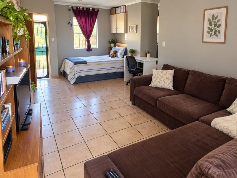 An open-plan living and bedroom area featuring tiled flooring, neutral wall tones, and direct access to an outdoor space via a security gate.