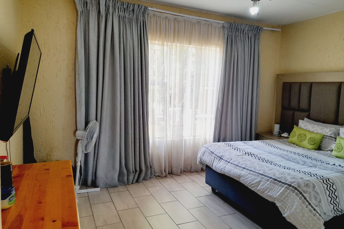 A well-lit bedroom featuring tiled flooring, a ceiling fan, and large windows dressed with floor-to-ceiling curtains.