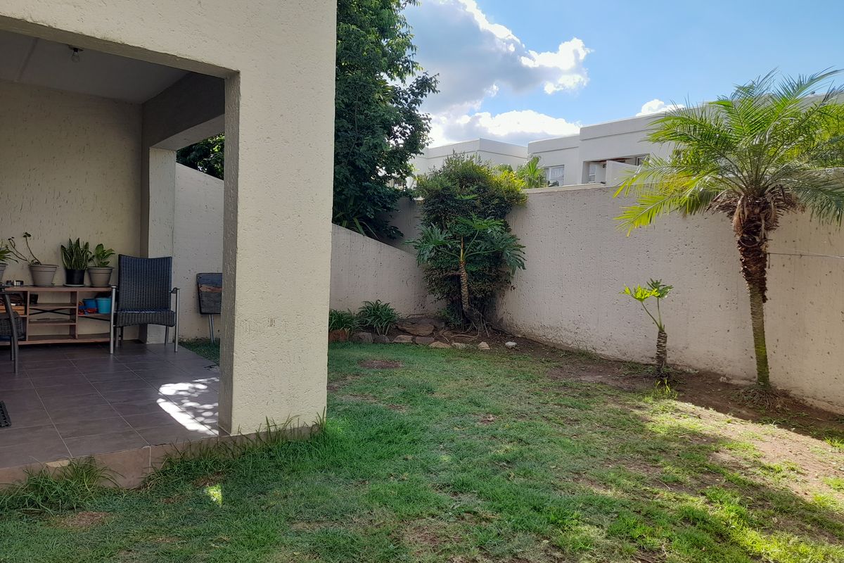 A private rear garden featuring a covered tiled patio area and a lawn enclosed by a high boundary wall.
