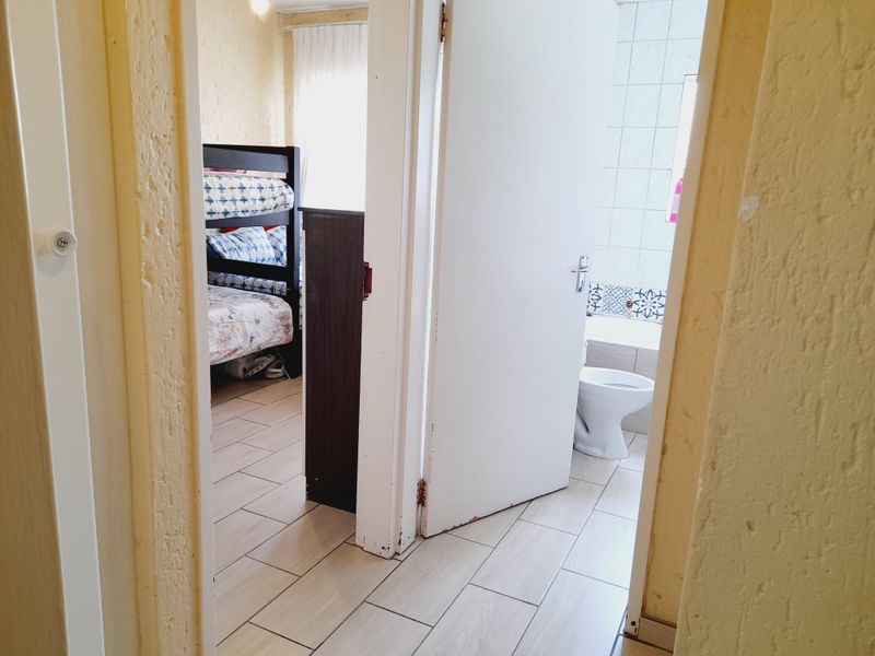 A view from a hallway looking into a bedroom and a bathroom, featuring tiled flooring and standard internal door frames.