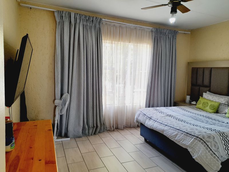 A bedroom featuring tiled flooring, a ceiling fan, and large windows dressed with curtains.