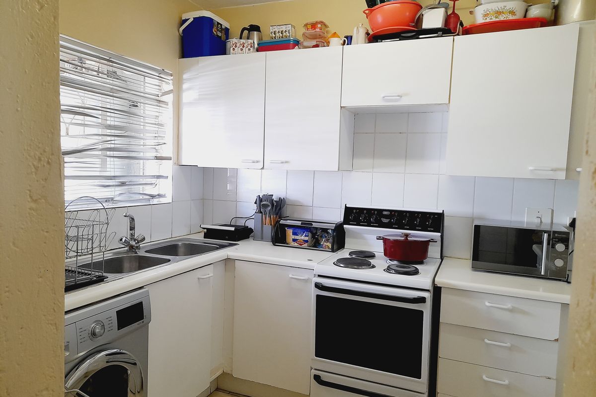 A functional kitchen featuring white cabinetry, tiled backsplash, double sink, and a freestanding stove, offering a practical layout for daily meal preparation.