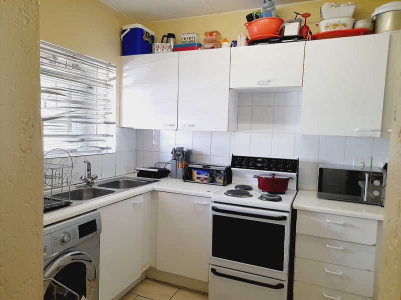 A functional kitchen featuring white cabinetry, tiled backsplash, double sink, and a freestanding stove, offering a practical layout for daily meal preparation.