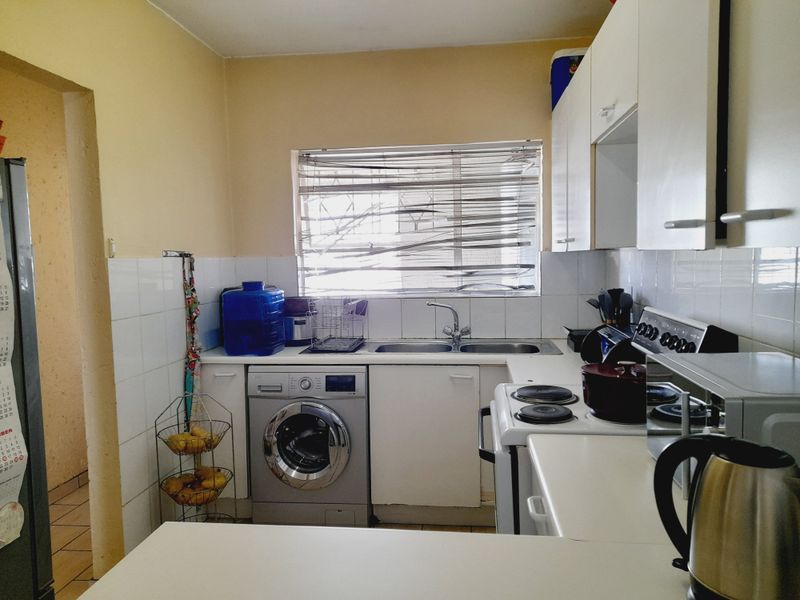 A functional kitchen featuring white cabinetry, tiled splashbacks, a double sink, and a freestanding stove with an integrated oven.