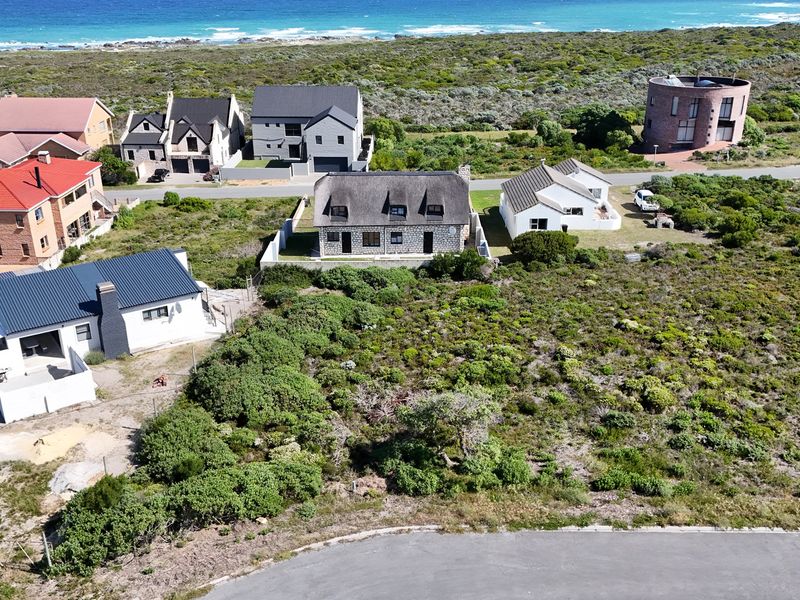 An aerial view of a coastal residential area featuring established homes, natural vegetation, and proximity to the ocean.