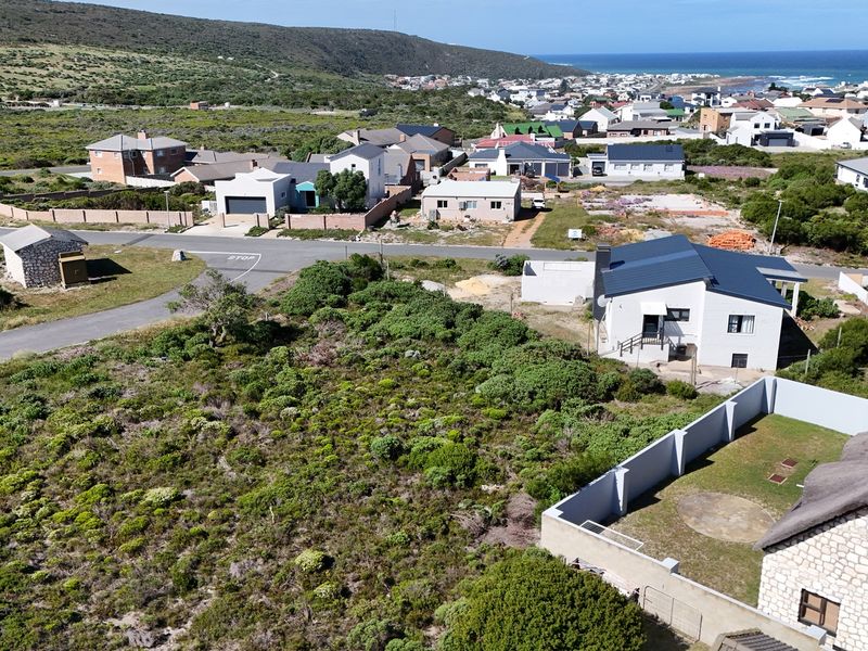Aerial view of a residential neighborhood and vacant land plot situated in a coastal area.