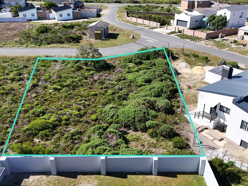 An aerial view of a vacant residential plot featuring natural vegetation and a boundary wall, situated in a developed neighborhood.