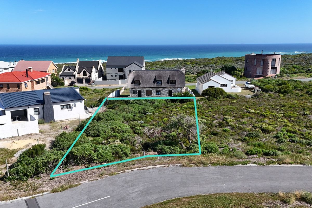 An aerial view of a vacant residential plot situated in a coastal neighborhood, featuring native vegetation and proximity to the ocean.