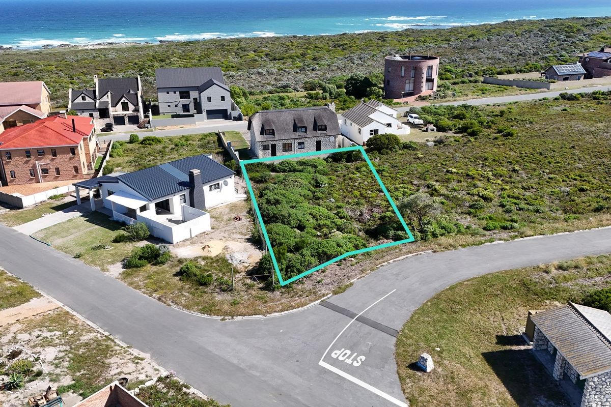 An aerial view of a vacant residential plot situated in a coastal neighborhood, featuring native vegetation and proximity to the ocean.