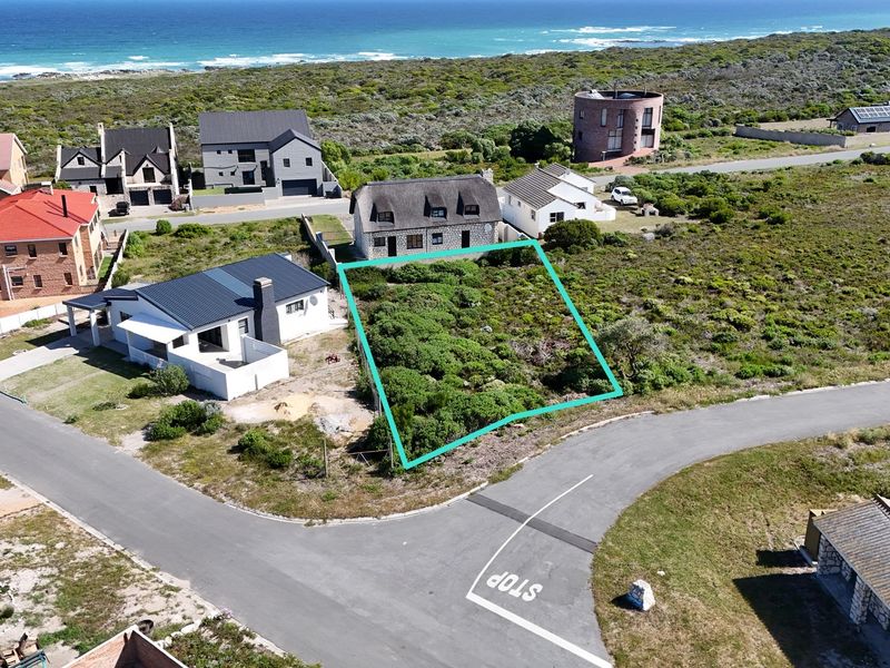 An aerial view of a vacant residential plot situated in a coastal neighborhood, featuring native vegetation and proximity to the ocean.