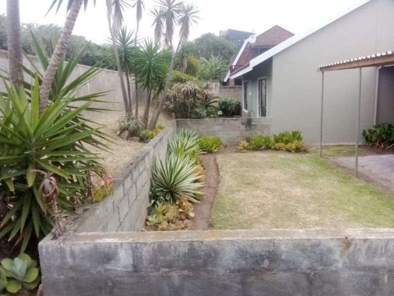 A rear garden area featuring a lawn, established landscaping, and concrete block retaining walls, adjacent to a covered patio space.