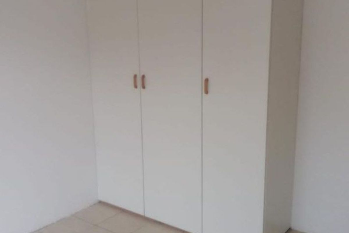 A simple bedroom featuring neutral tiled flooring and white built-in cupboards providing ample storage space.