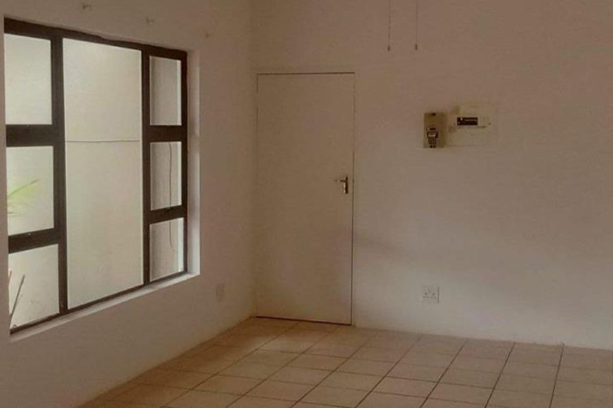 An empty living room featuring tiled flooring, a ceiling fan, and a large window, providing a blank canvas for interior design.