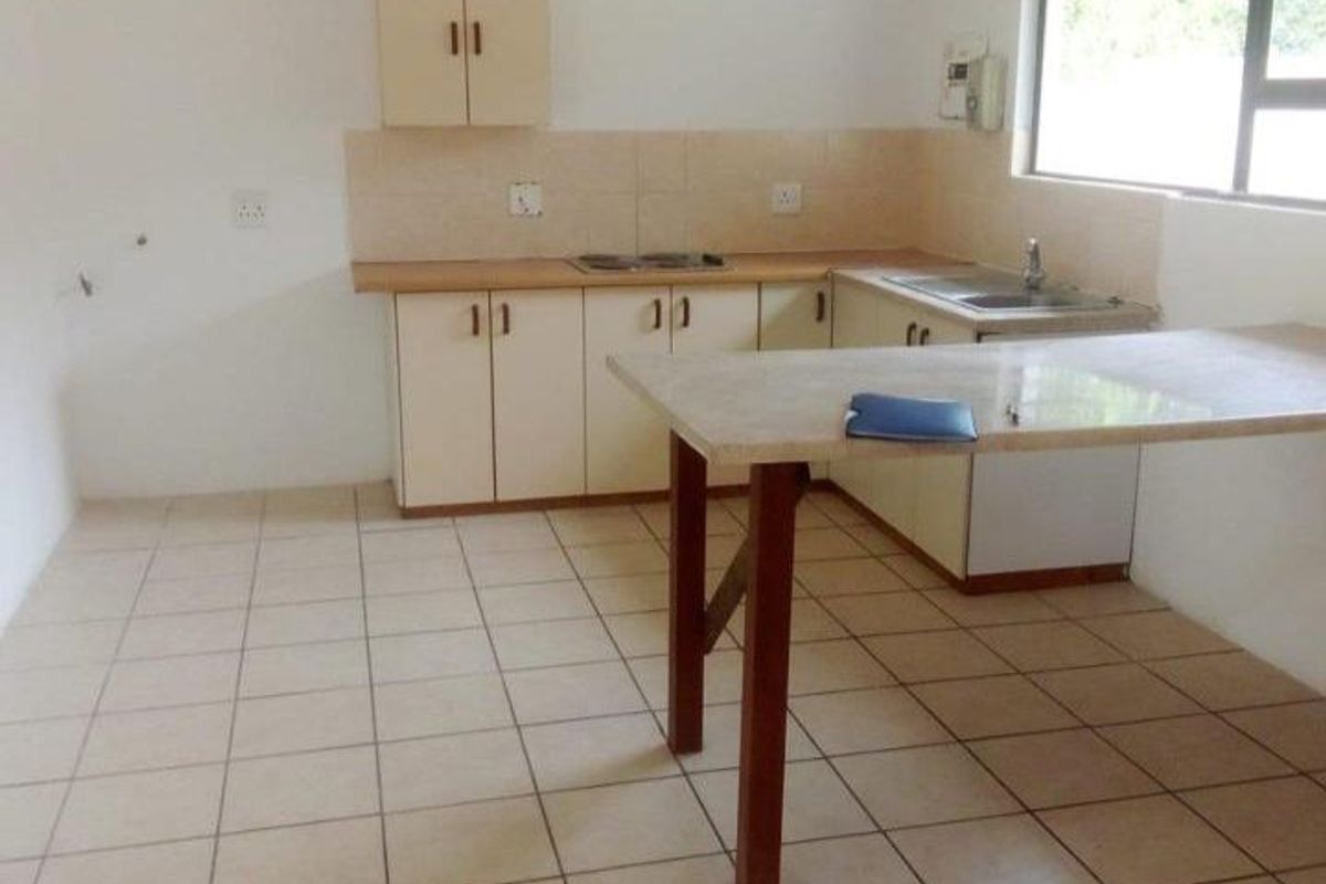 A functional, empty kitchen featuring tiled flooring, built-in cabinetry, a laminate countertop with an integrated sink, and a built-in hob.