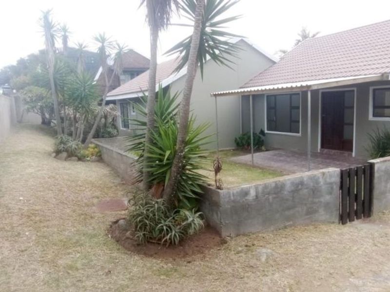 Rear view of the townhouse featuring a covered patio, tiled roof, and a private garden area enclosed by a concrete block boundary wall.