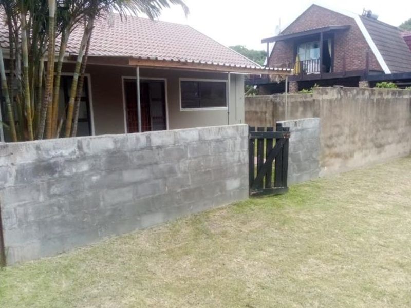 Rear view of the townhouse featuring a small lawn, a covered patio area, and a concrete block boundary wall with a timber gate.