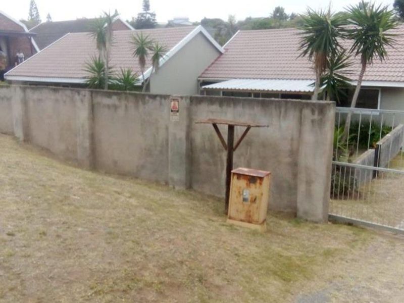 Front exterior view of a townhouse featuring a concrete boundary wall, tiled roof, and gated entrance with a weathered utility box.