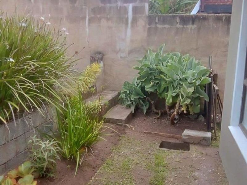 A rear exterior area featuring a concrete block retaining wall and garden beds requiring landscaping and maintenance.