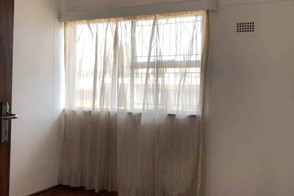An empty bedroom featuring classic parquet flooring, a ceiling pendant light, and a window with security bars.