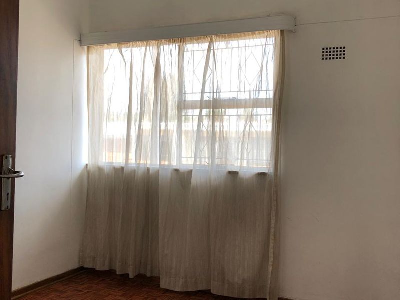An empty bedroom featuring classic parquet flooring, a ceiling pendant light, and a window with security bars.