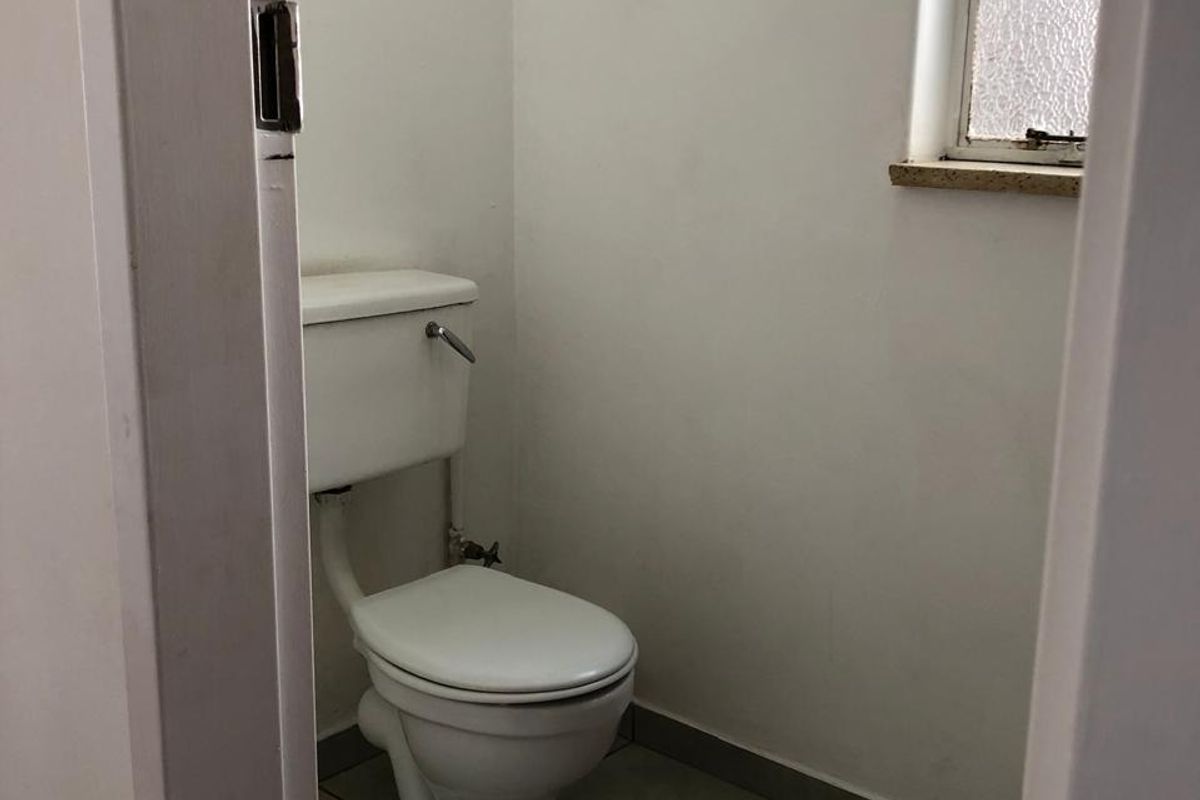 A compact, functional bathroom featuring a standard toilet, tiled flooring, and an obscured glass window for privacy.