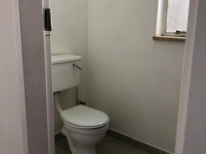 A compact, functional bathroom featuring a standard toilet, tiled flooring, and an obscured glass window for privacy.