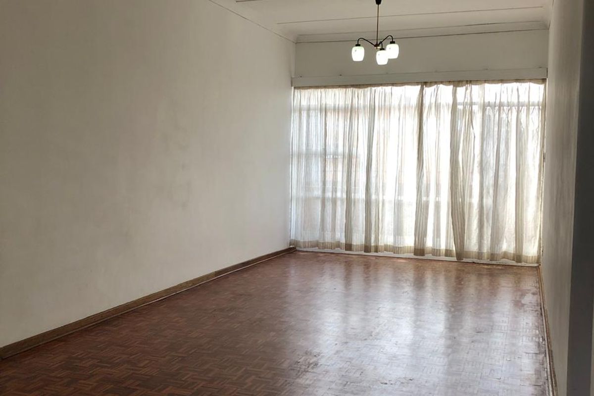 Spacious, empty living room featuring original parquet flooring, coved ceilings, and dual pendant light fixtures, offering a blank canvas for renovation.