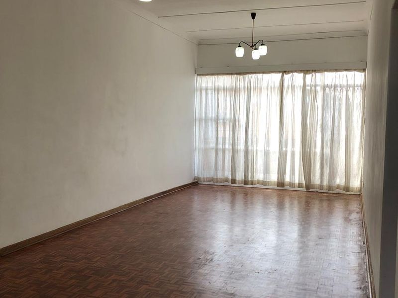 Spacious, empty living room featuring original parquet flooring, coved ceilings, and dual pendant light fixtures, offering a blank canvas for renovation.