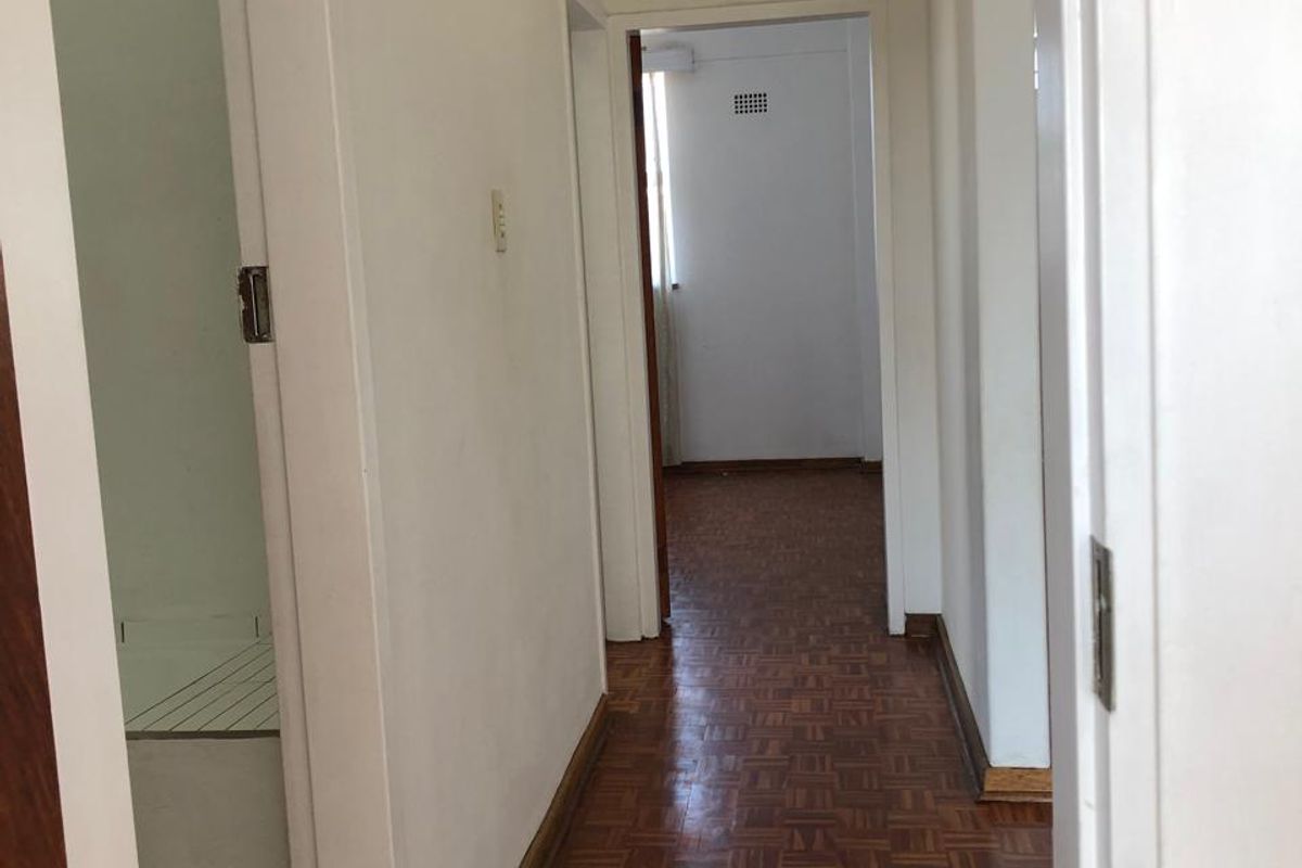 A clean, empty hallway featuring traditional parquet flooring and white walls, providing access to multiple rooms within the apartment.