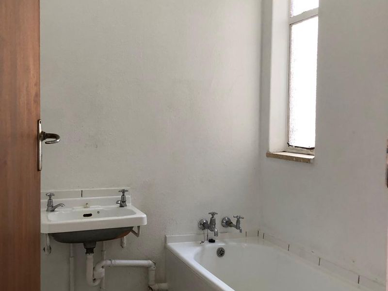 A functional bathroom featuring a wall-mounted basin, a built-in bathtub, and tiled flooring, offering a blank canvas for potential modernization and renovation.