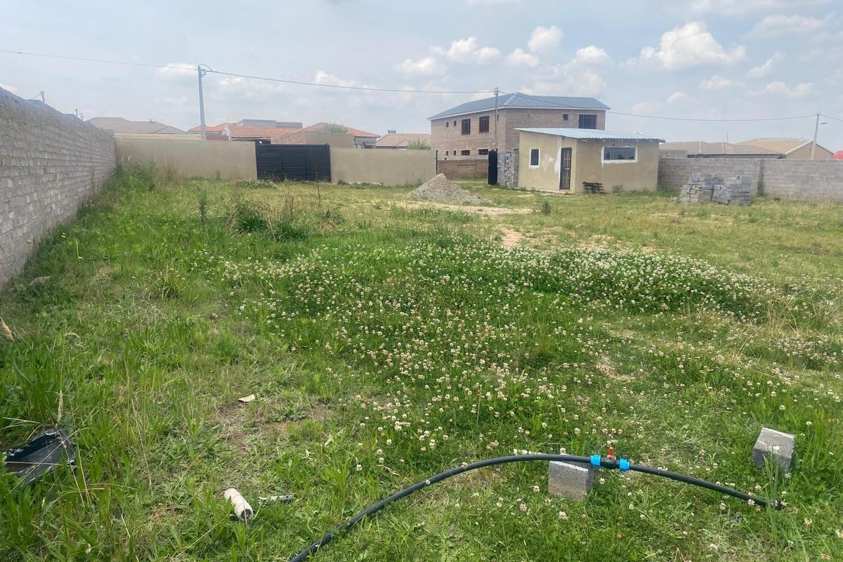 A vacant residential plot featuring a perimeter wall, an existing outbuilding, and open grass area, suitable for future development.